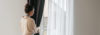 Young woman standing near the widnow and fixing the curtains